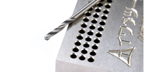 Close-up of a micro-drill positioned above a precision-drilled metal component, illustrating the need for specialist tooling solutions to achieve high-density, micron-level accuracy in advanced manufacturing applications.