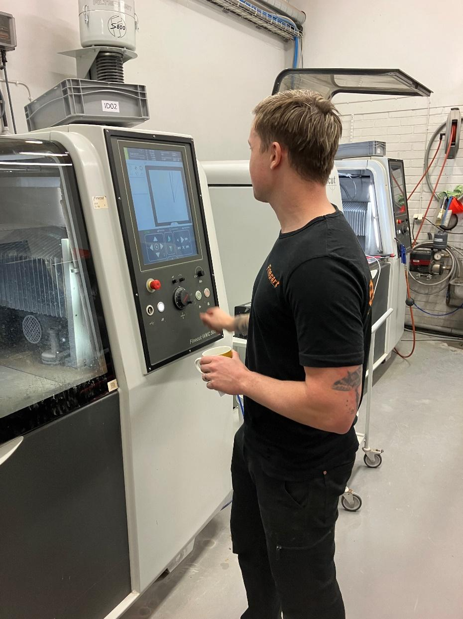 Technician operating a CNC micro abrasive waterjet cutting machine in a precision engineering workshop, demonstrating advanced manufacturing technology for intricate component production.